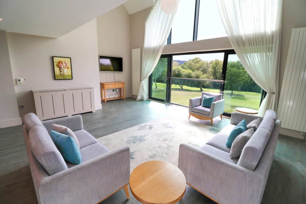 Bright lounge with large windows overlooking lush green golf course scenery.