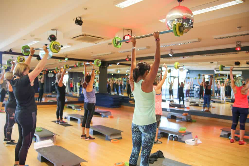 Group fitness class at Old Thorns with participants lifting weights overhead.