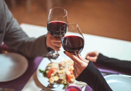 couple with red wine in glasses over a plate of food